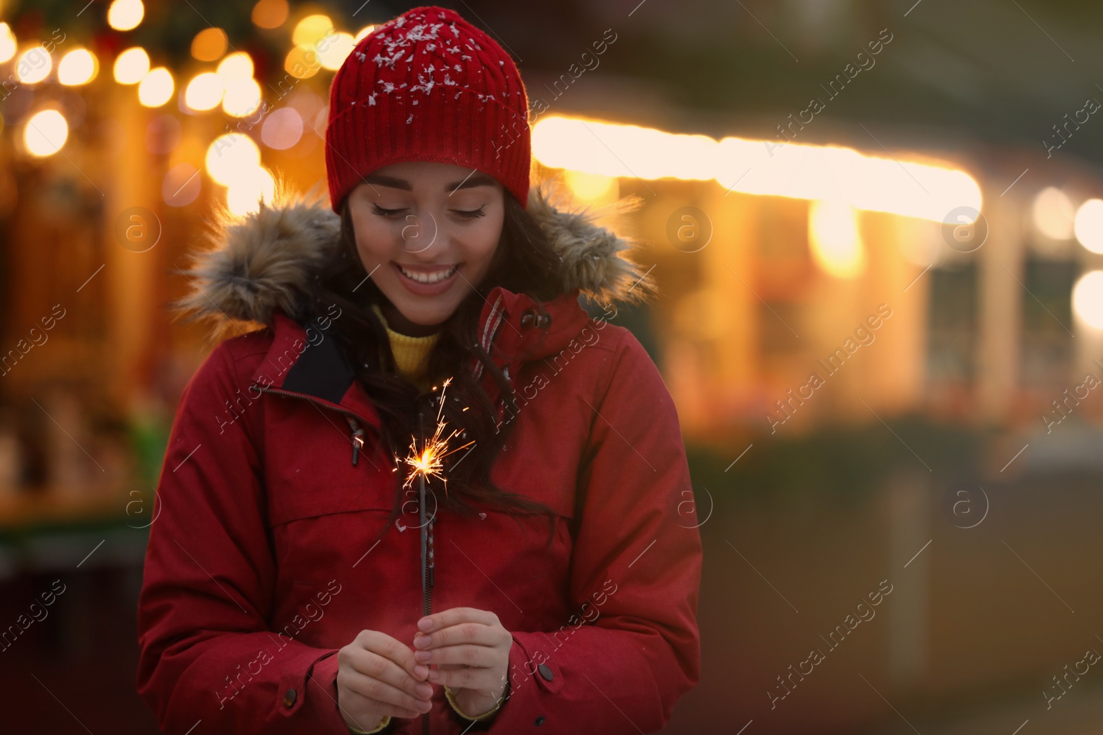 Photo of Happy young woman with sparkler at winter fair in evening. Christmas celebration