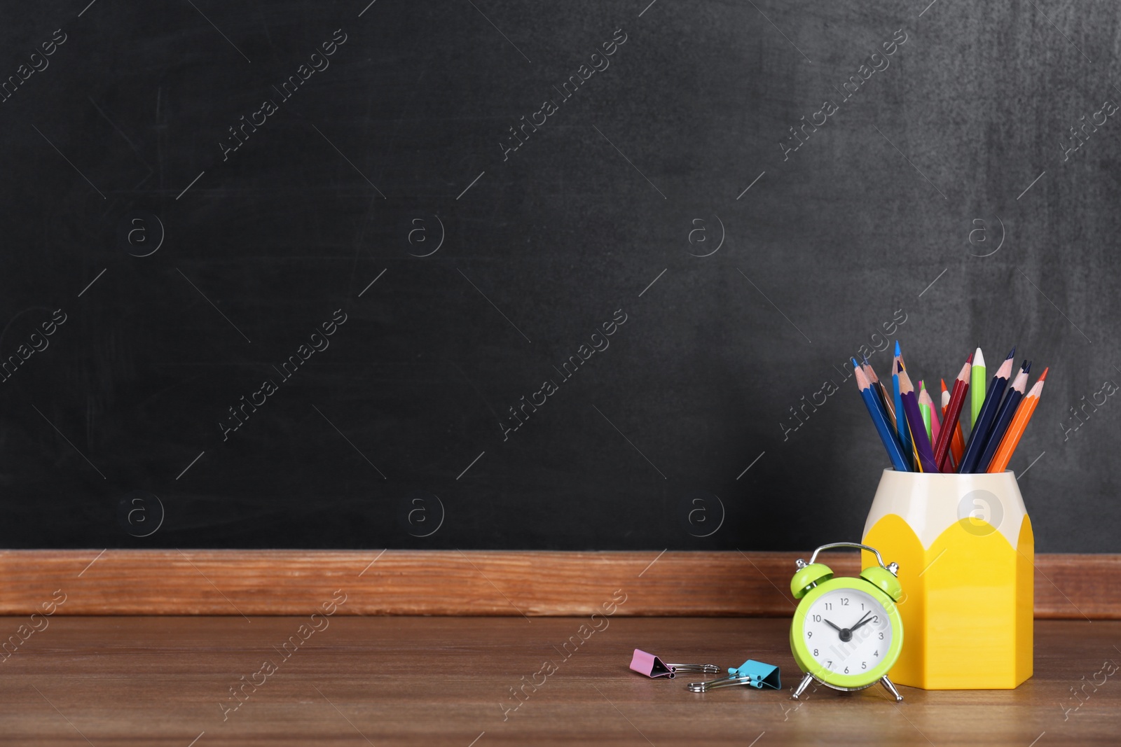 Photo of Pencils and alarm clock on wooden table near blackboard, space for text. Doing homework