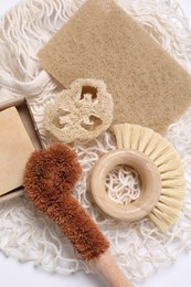 Cleaning brushes, sponge, loofah and soap bar on white table, top view