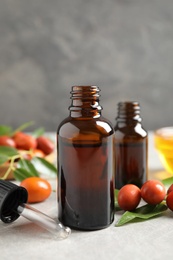 Photo of Glass bottles with jojoba oil and seeds on stone table against grey background