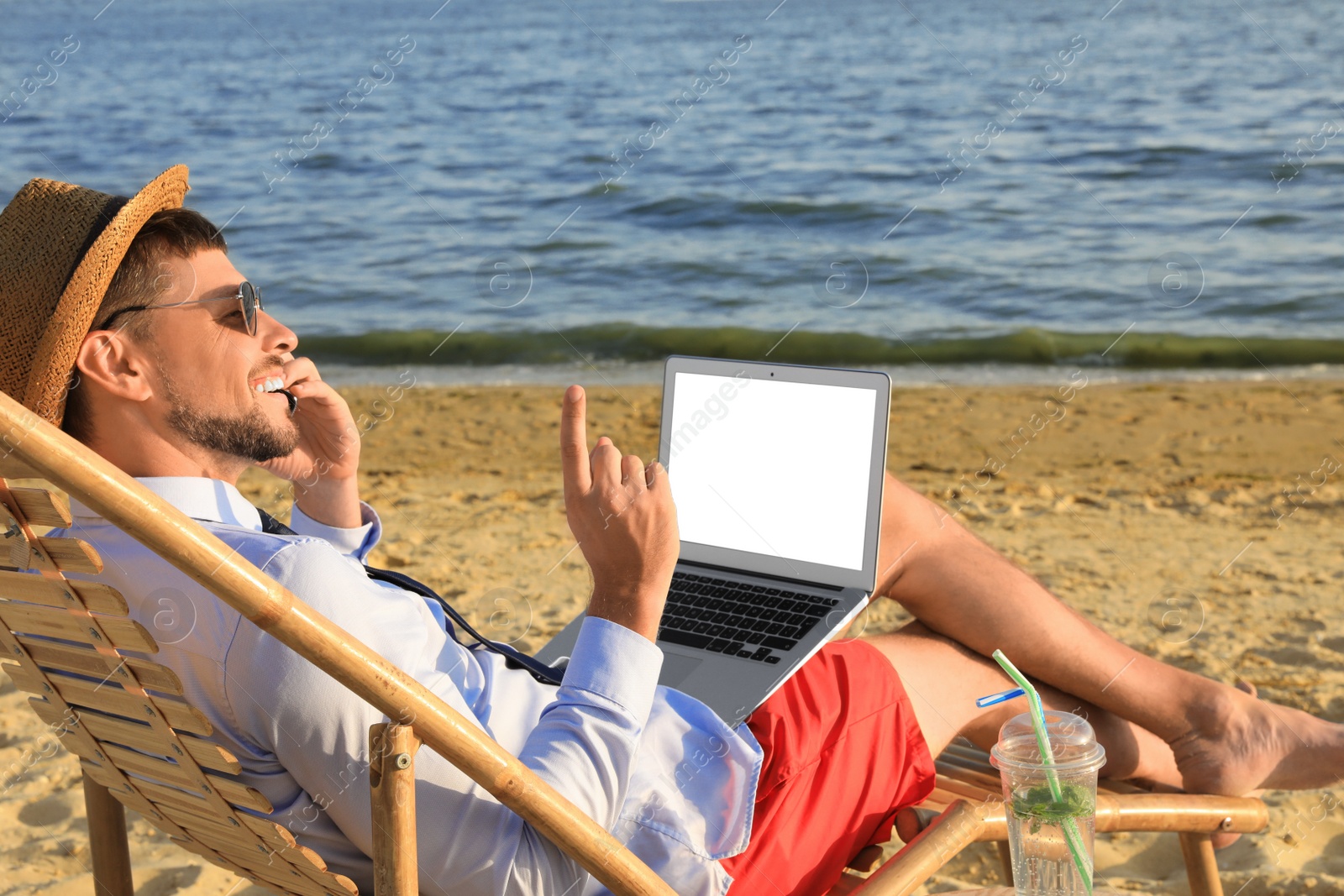 Photo of Man with laptop talking by mobile phone on beach. Business trip