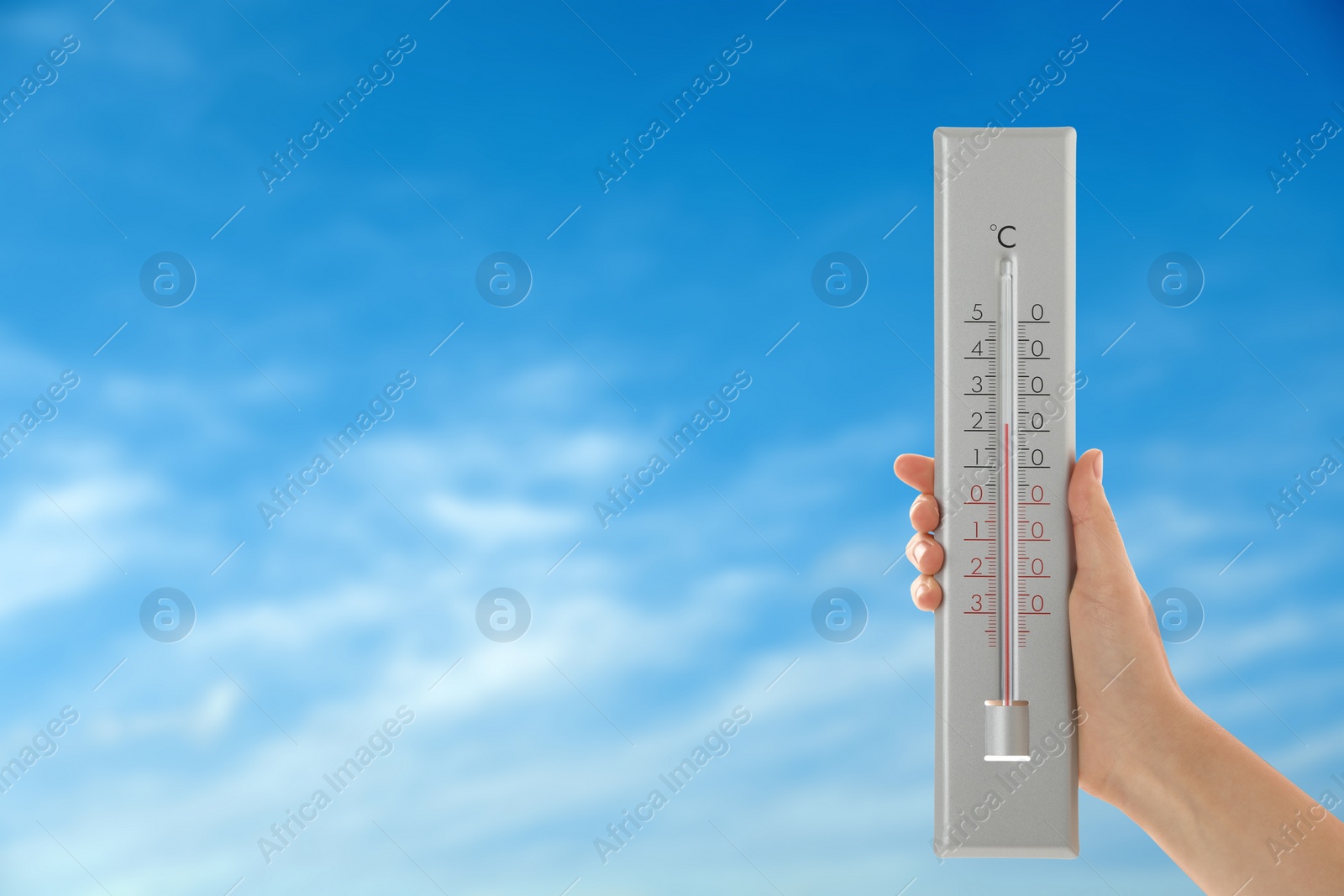 Image of Woman holding thermometer against blue sky, closeup. Space for text