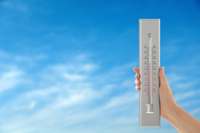 Image of Woman holding thermometer against blue sky, closeup. Space for text