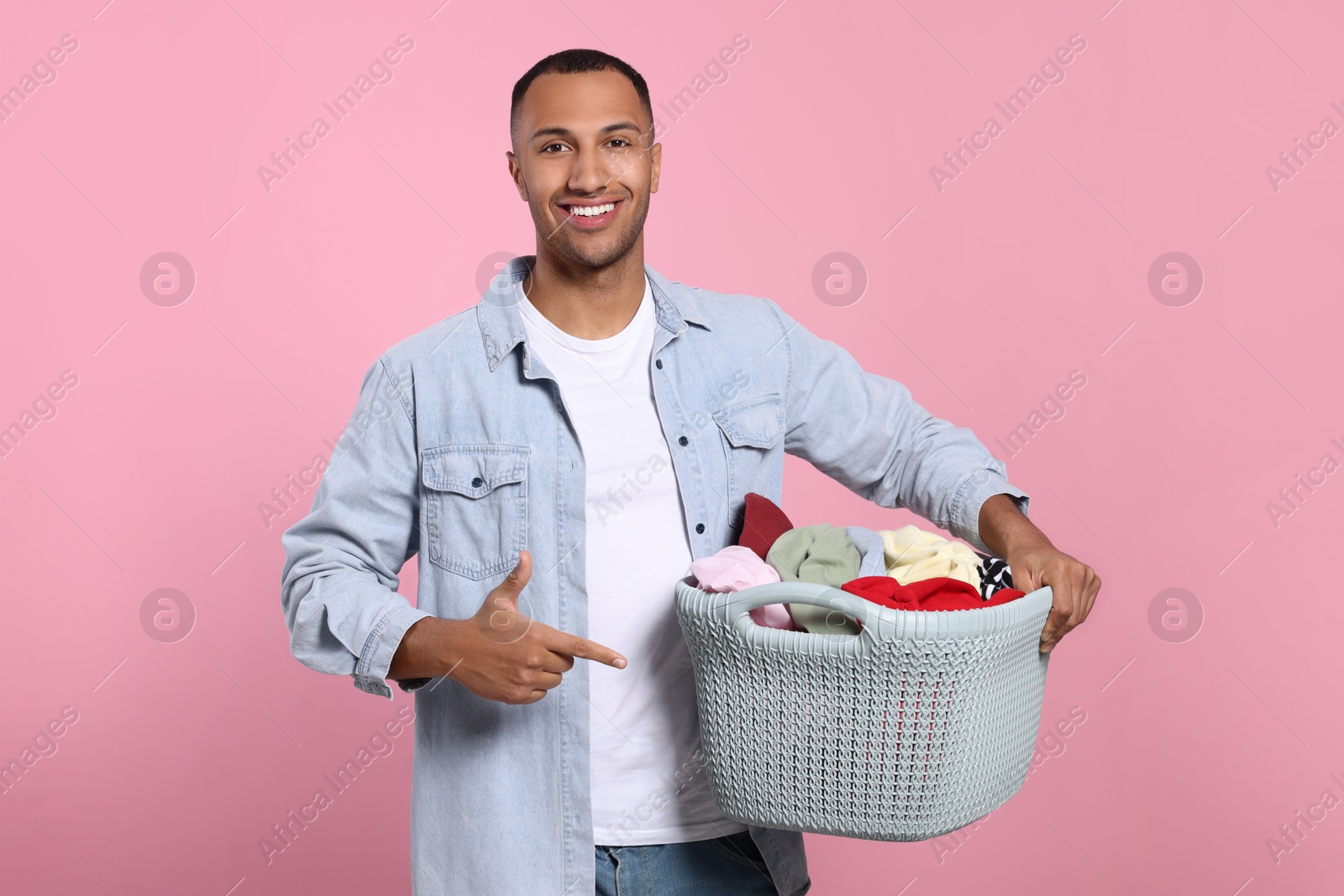 Photo of Happy man with basket full of laundry on pink background