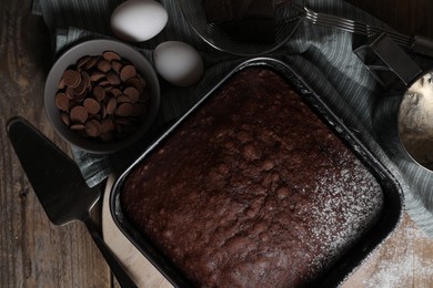 Homemade chocolate sponge cake and ingredients on wooden table, flat lay