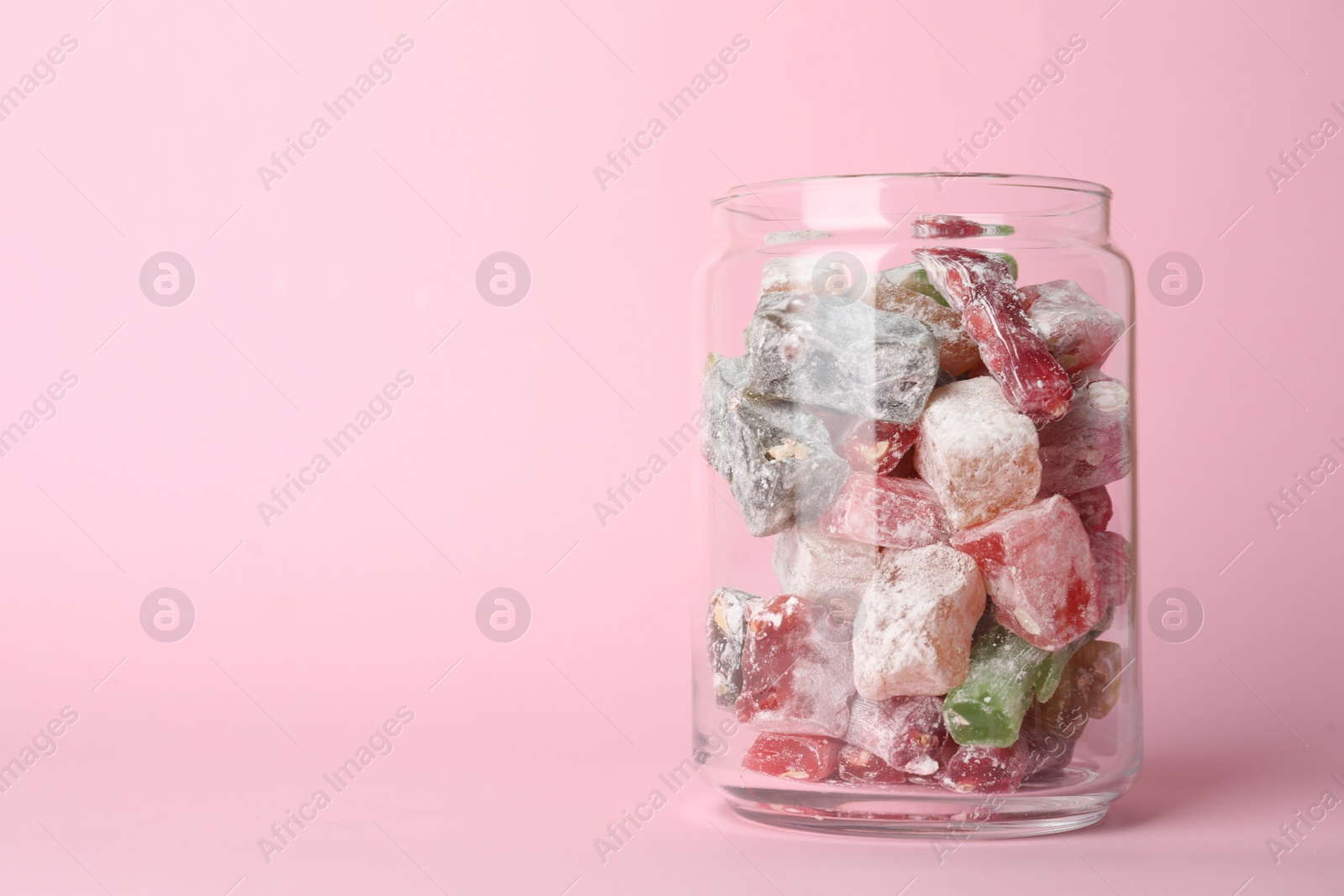 Photo of Delicious candies in glass jar on pink background. Space for text