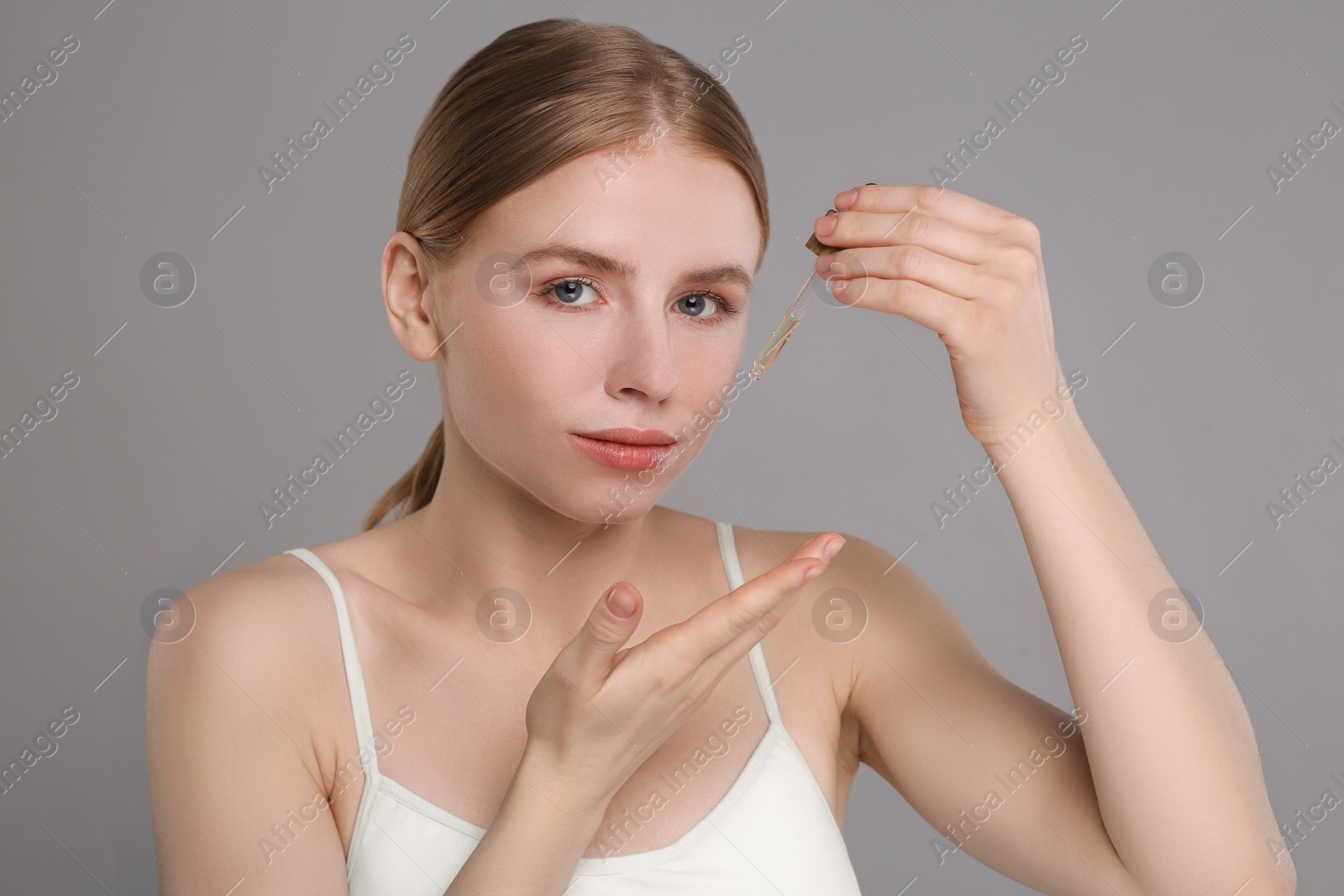 Photo of Beautiful young woman applying essential oil onto face on grey background