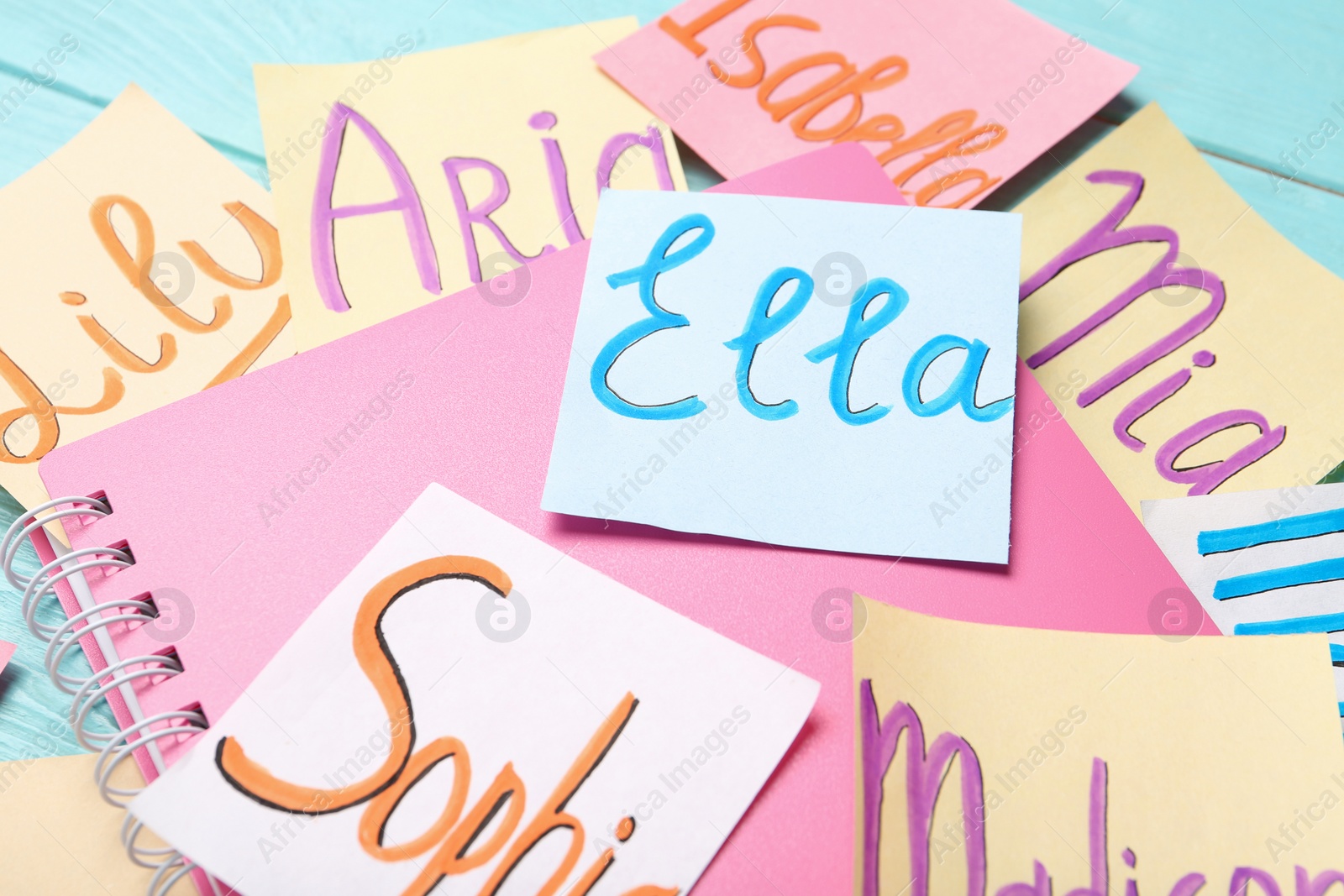 Photo of Paper notes with different baby names and notebook on light blue wooden table, closeup