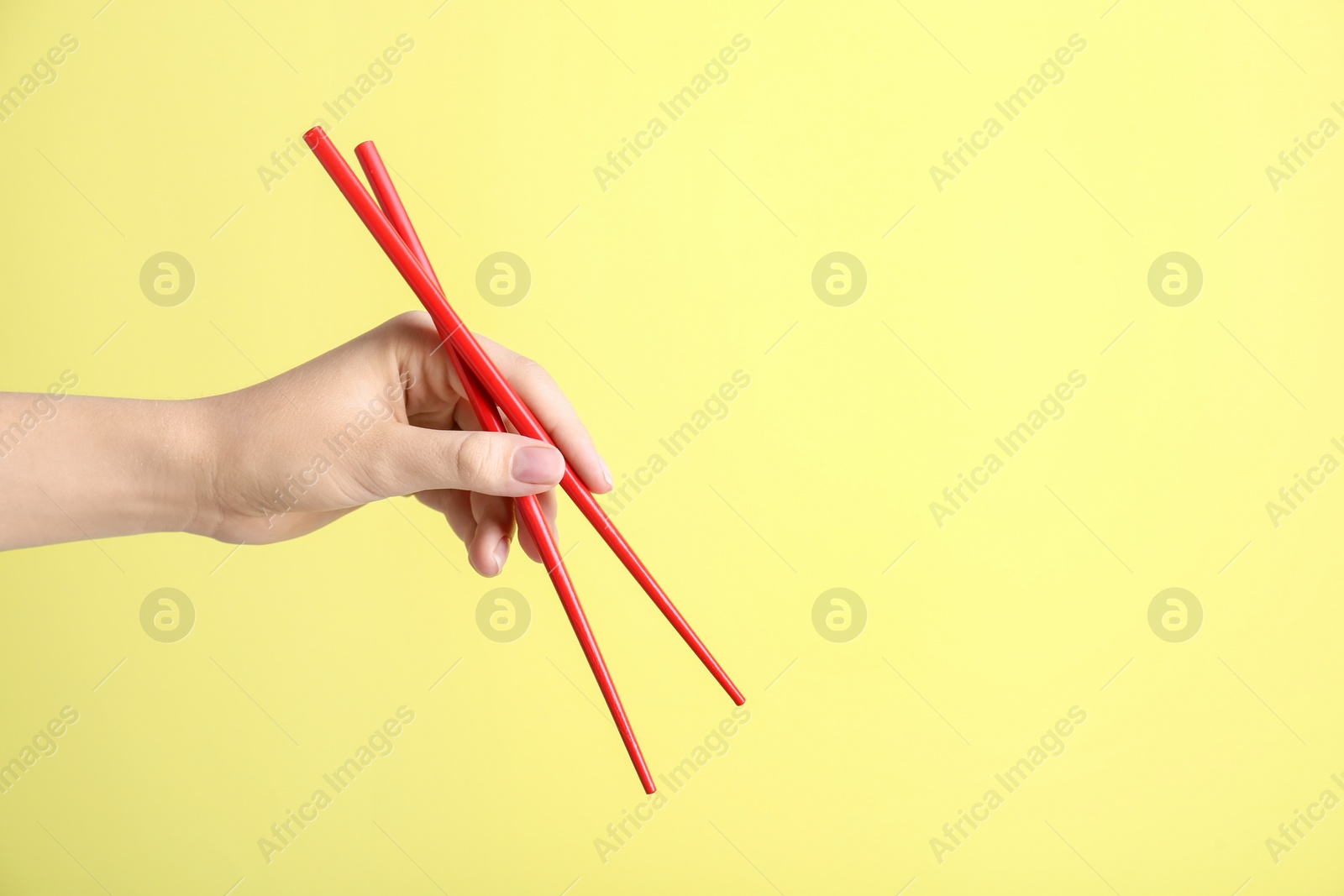 Photo of Woman holding pair of red chopsticks on yellow background, closeup. Space for text