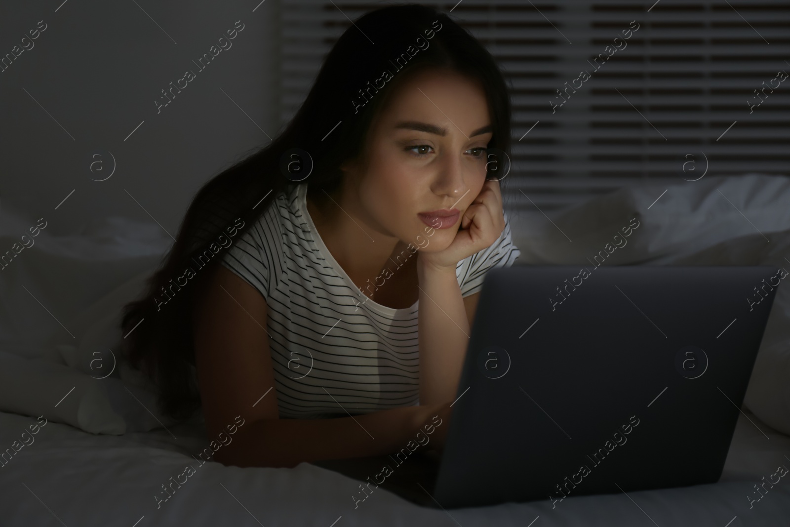 Photo of Young woman using laptop in dark bedroom