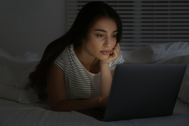 Young woman using laptop in dark bedroom