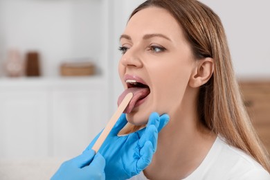 Photo of Doctor examining woman`s oral cavity with tongue depressor indoors