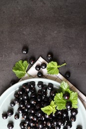 Plate with ripe blackcurrants and leaves on grey background, flat lay. Space for text