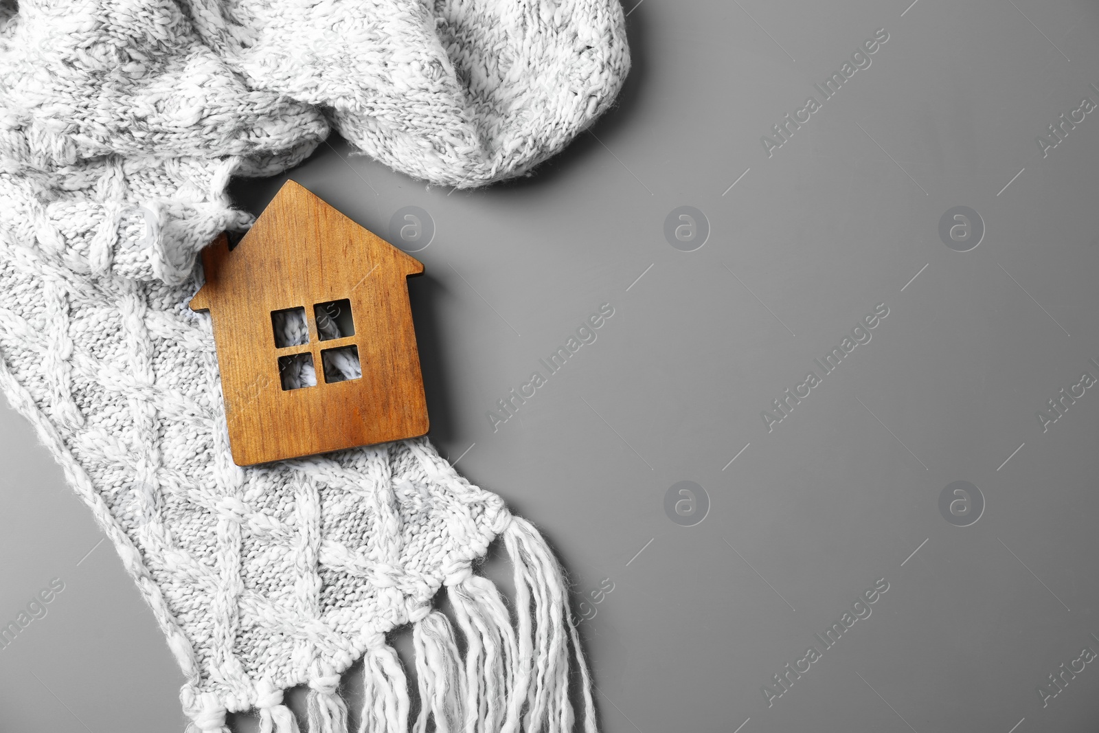 Photo of Wooden house model and scarf on grey background, top view with space for text. Heating efficiency