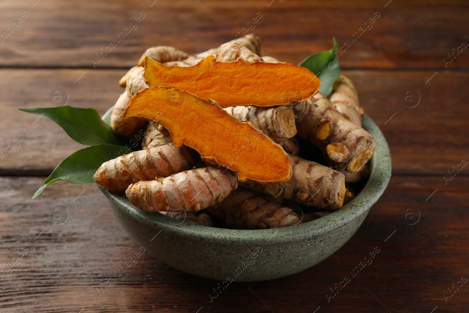 Photo of Bowl with fresh turmeric roots on wooden table, closeup