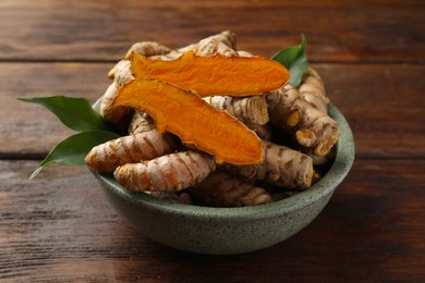 Bowl with fresh turmeric roots on wooden table, closeup