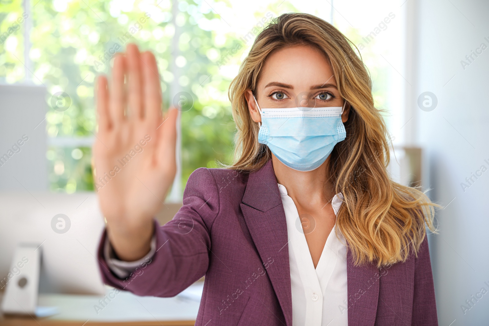 Photo of Woman in protective face mask showing stop gesture in office. Prevent spreading of coronavirus