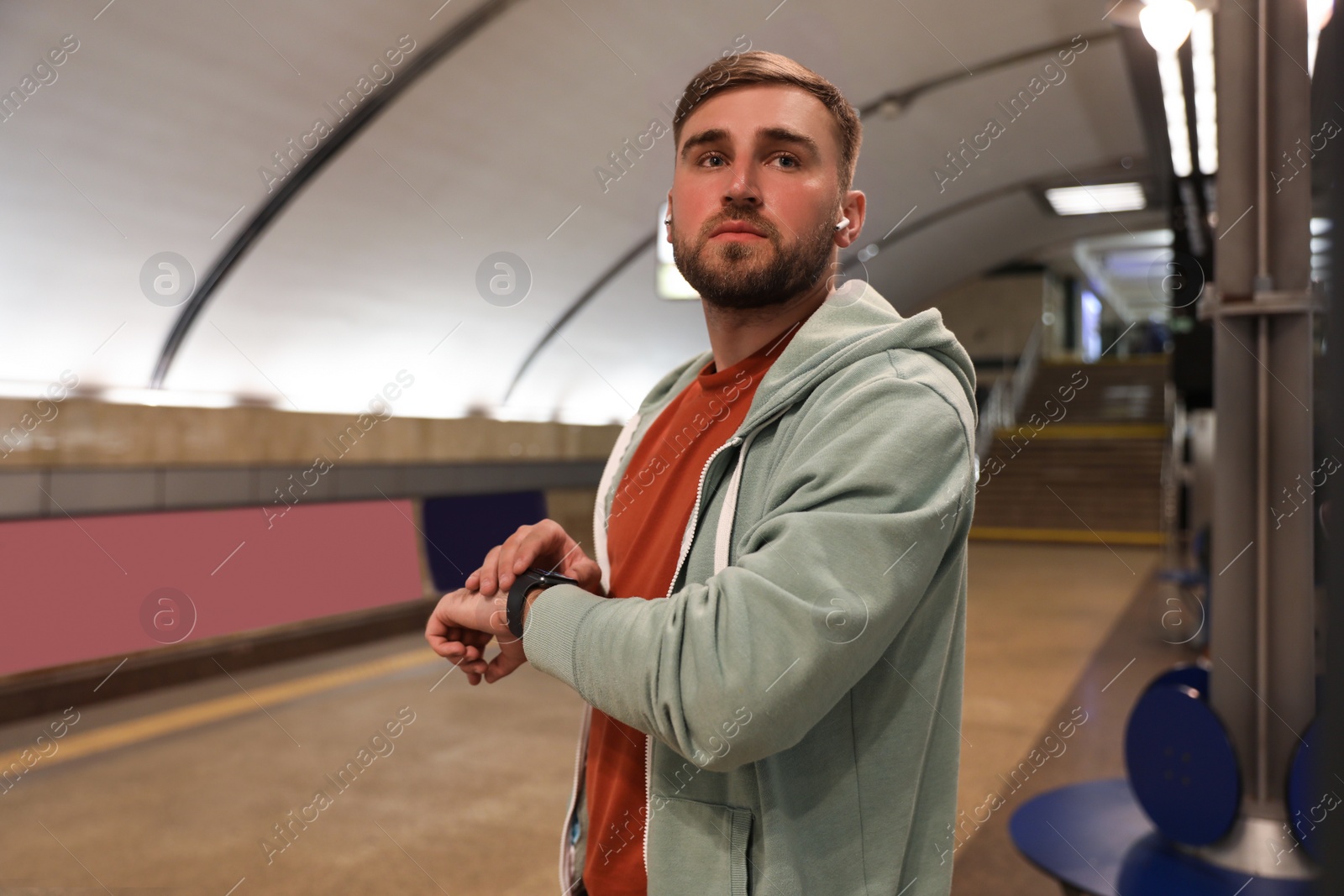 Photo of Young man with earphones waiting for train at subway station. Public transport