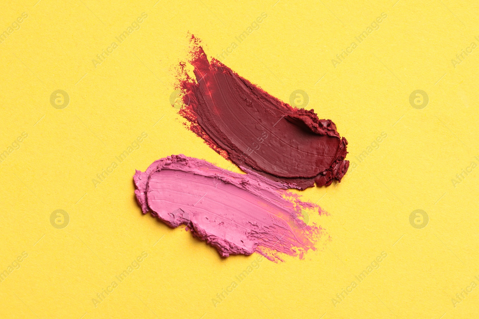 Photo of Smears of bright lipsticks on yellow background, top view