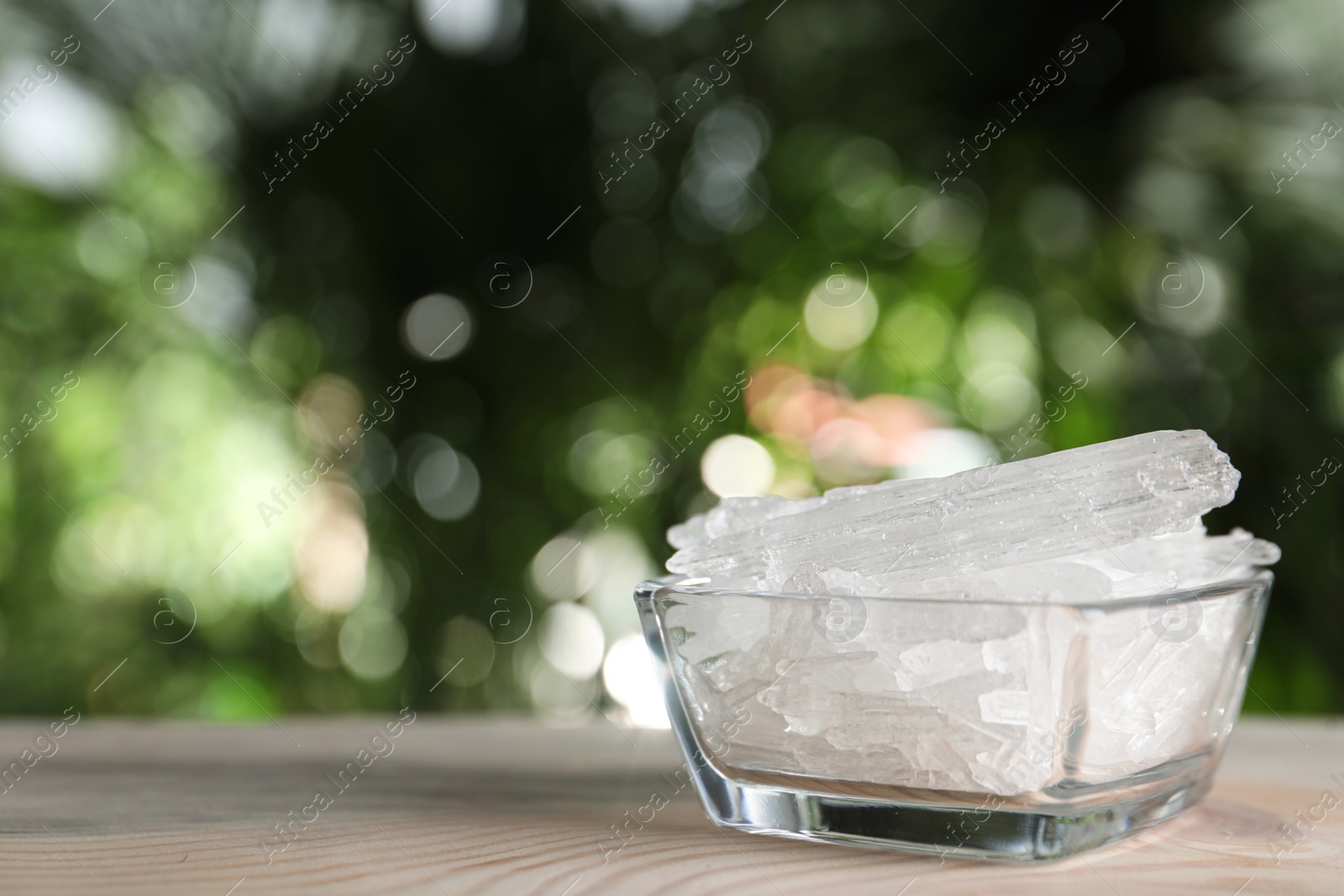 Photo of Menthol crystals in glass bowl on wooden table against blurred background. Space for text