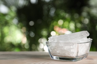 Photo of Menthol crystals in glass bowl on wooden table against blurred background. Space for text