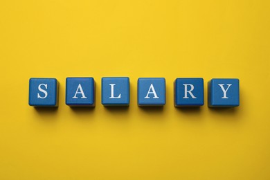 Image of Word Salary made with blue wooden cubes on yellow background, flat lay