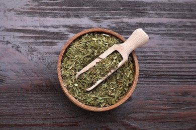 Bowl of dry tarragon and scoop on wooden table, top view