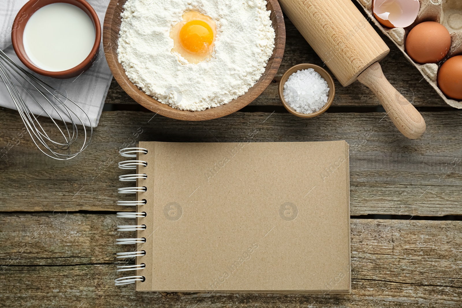 Photo of Blank recipe book and different ingredients on wooden table, flat lay. Space for text