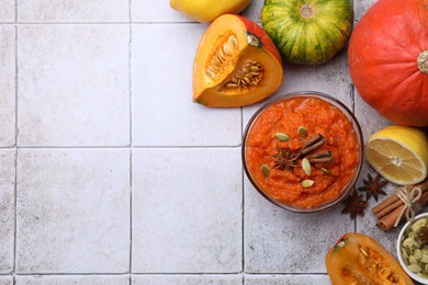 Photo of Bowl of delicious pumpkin jam and ingredients on tiled surface, flat lay. Space for text