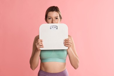 Photo of Woman in sportswear with scales on pink background