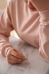 Photo of Woman holding wedding ring at table indoors, closeup. Divorce concept