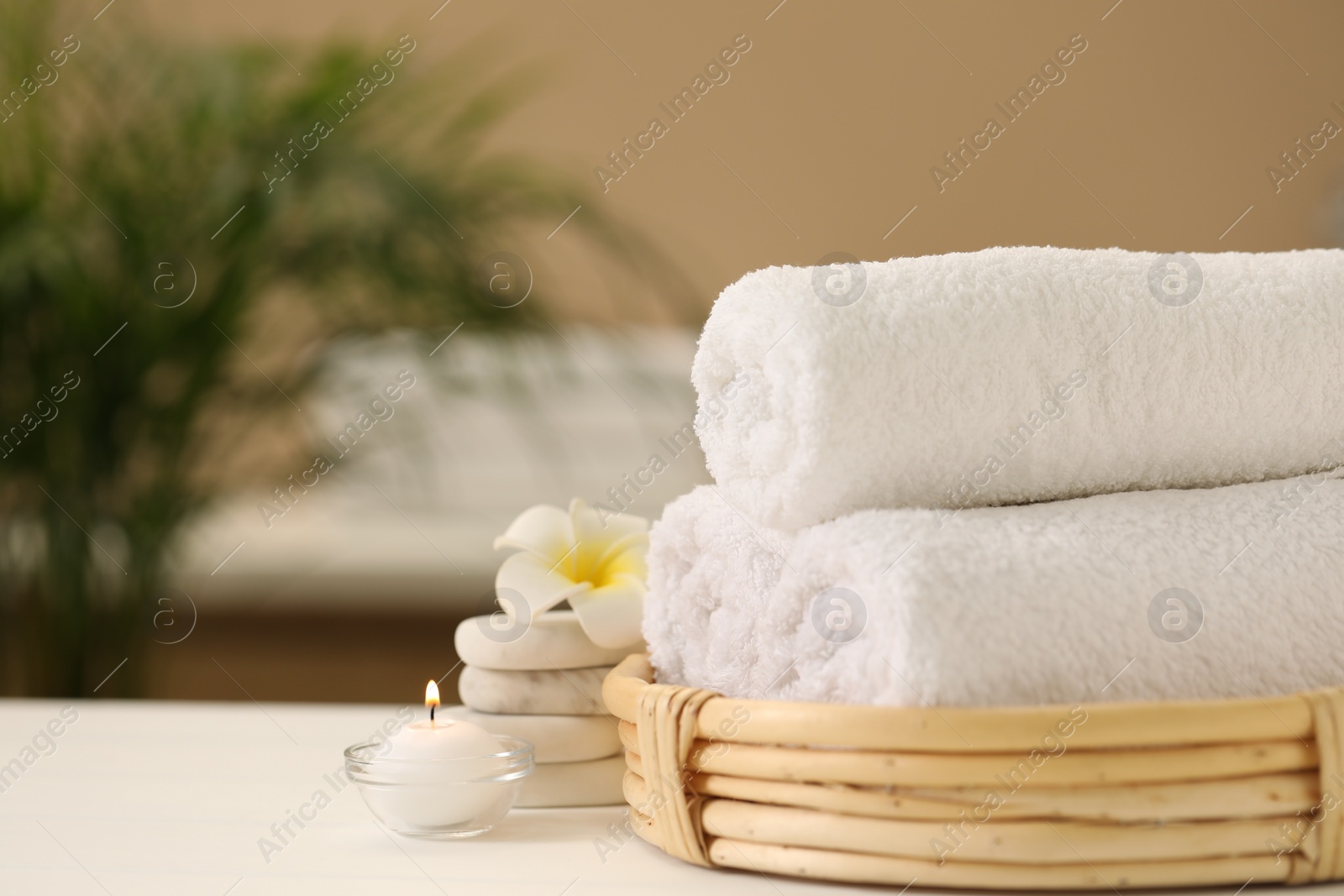 Photo of Spa composition. Rolled towels, massage stones, burning candle and plumeria flower on table. Space for text