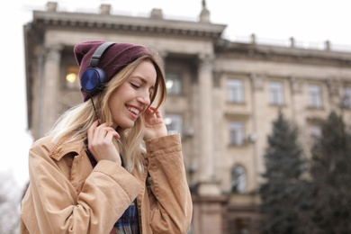 Photo of Young woman with headphones listening to music outdoors. Space for text