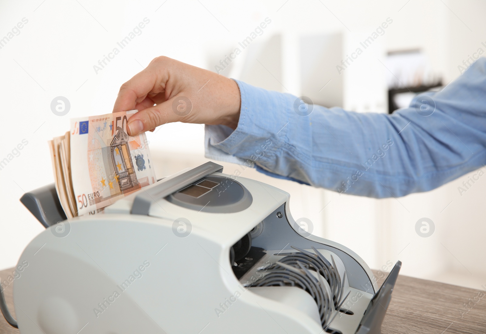 Photo of Female teller putting money into currency counting machine at cash department, closeup