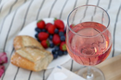 Photo of Glass of delicious rose wine and food on white picnic blanket, closeup
