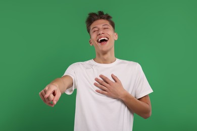 Young man pointing at something and laughing on green background