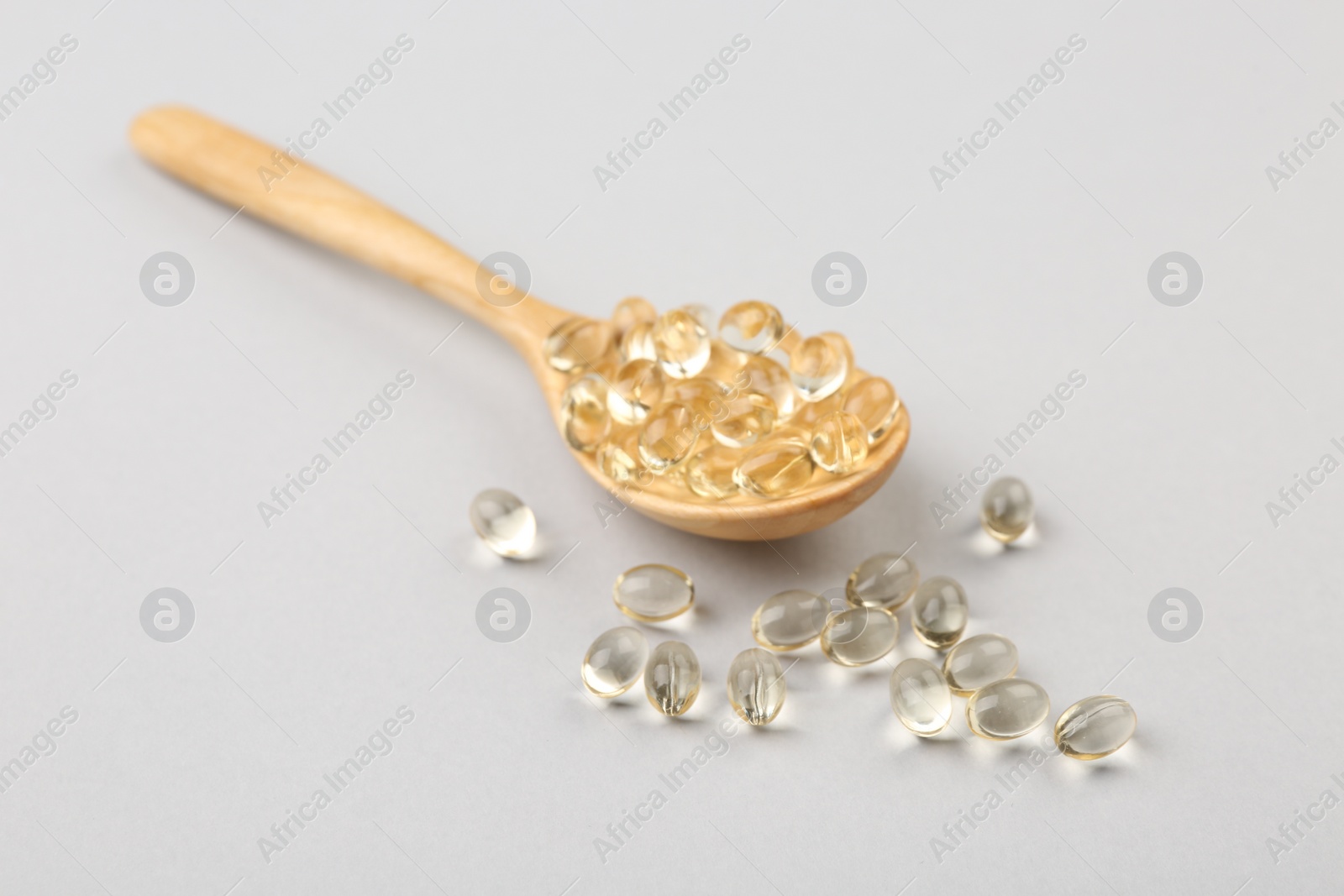Photo of Wooden spoon with vitamin capsules on light background, closeup