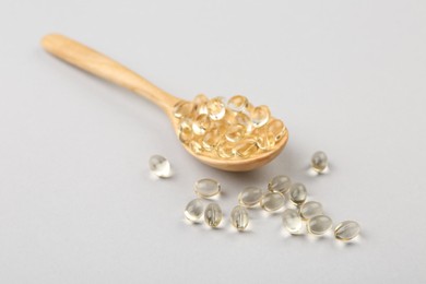 Wooden spoon with vitamin capsules on light background, closeup