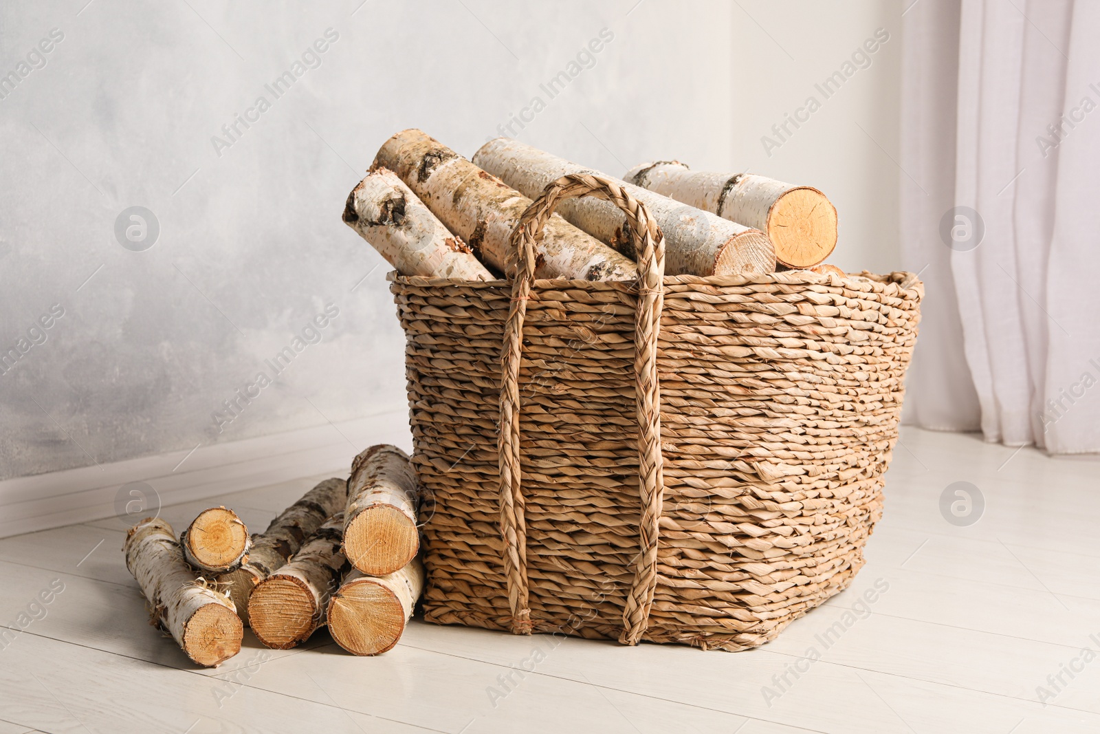 Photo of Wicker basket with cut firewood on white floor indoors