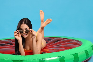 Photo of Young woman in stylish sunglasses on inflatable mattress against light blue background