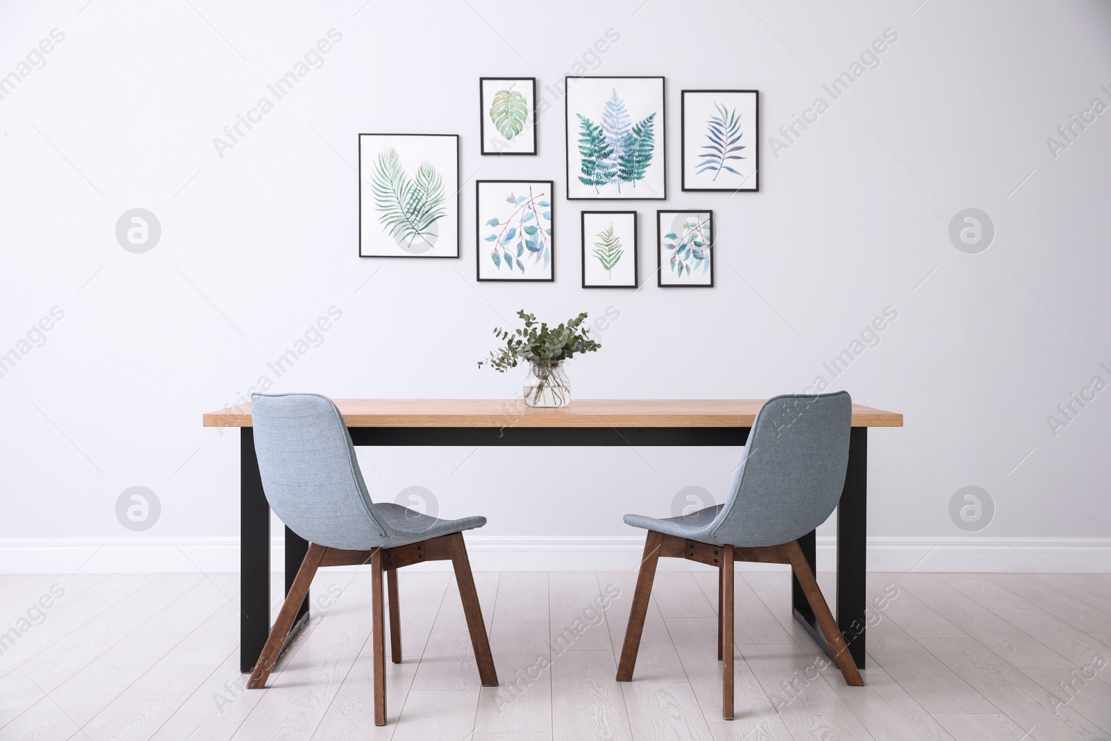 Photo of Stylish room interior with modern table, chairs and paintings of tropical leaves. Idea for design