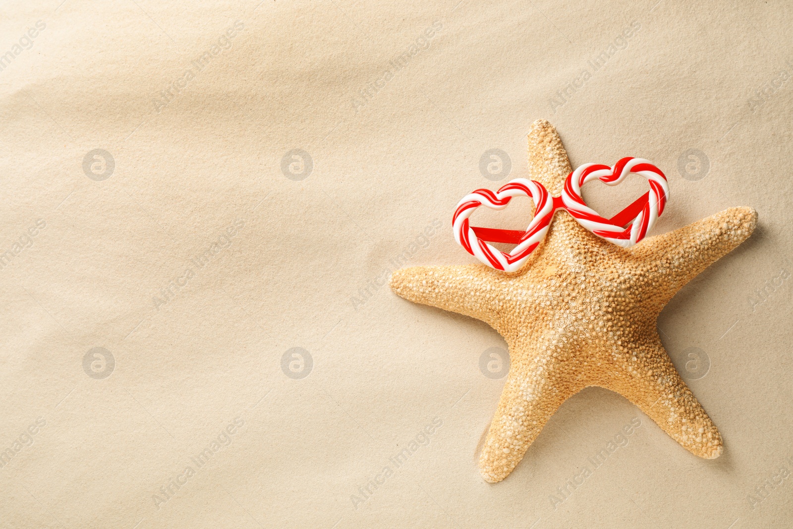 Photo of Beautiful starfish with candy cane party sunglasses and space for text on sand, top view. Christmas vacation