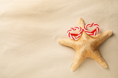 Beautiful starfish with candy cane party sunglasses and space for text on sand, top view. Christmas vacation