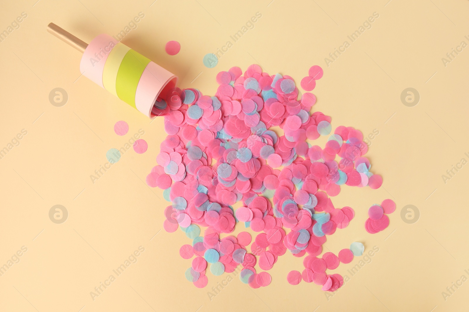 Photo of Colorful confetti bursting out of party popper on beige background, flat lay