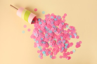 Photo of Colorful confetti bursting out of party popper on beige background, flat lay