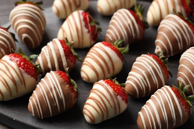 Photo of Delicious chocolate covered strawberries on black board, closeup