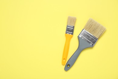 Photo of Two paint brushes on pale yellow background, flat lay. Space for text