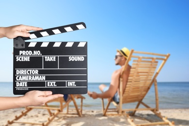 Image of Assistant holding clapperboard and people relaxing in deck chairs on beach, closeup. Cinema production 