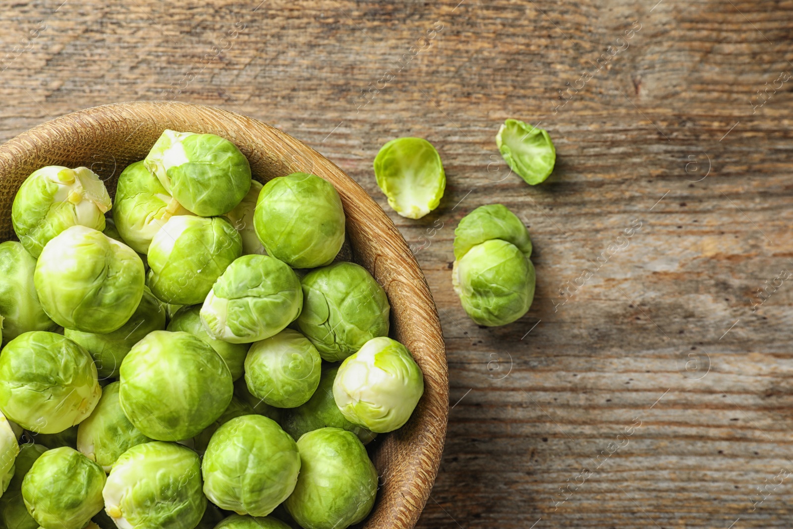 Photo of Bowl of fresh Brussels sprouts on wooden background, top view with space for text