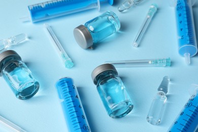 Photo of Disposable syringes with needles, ampules and vials on light blue background